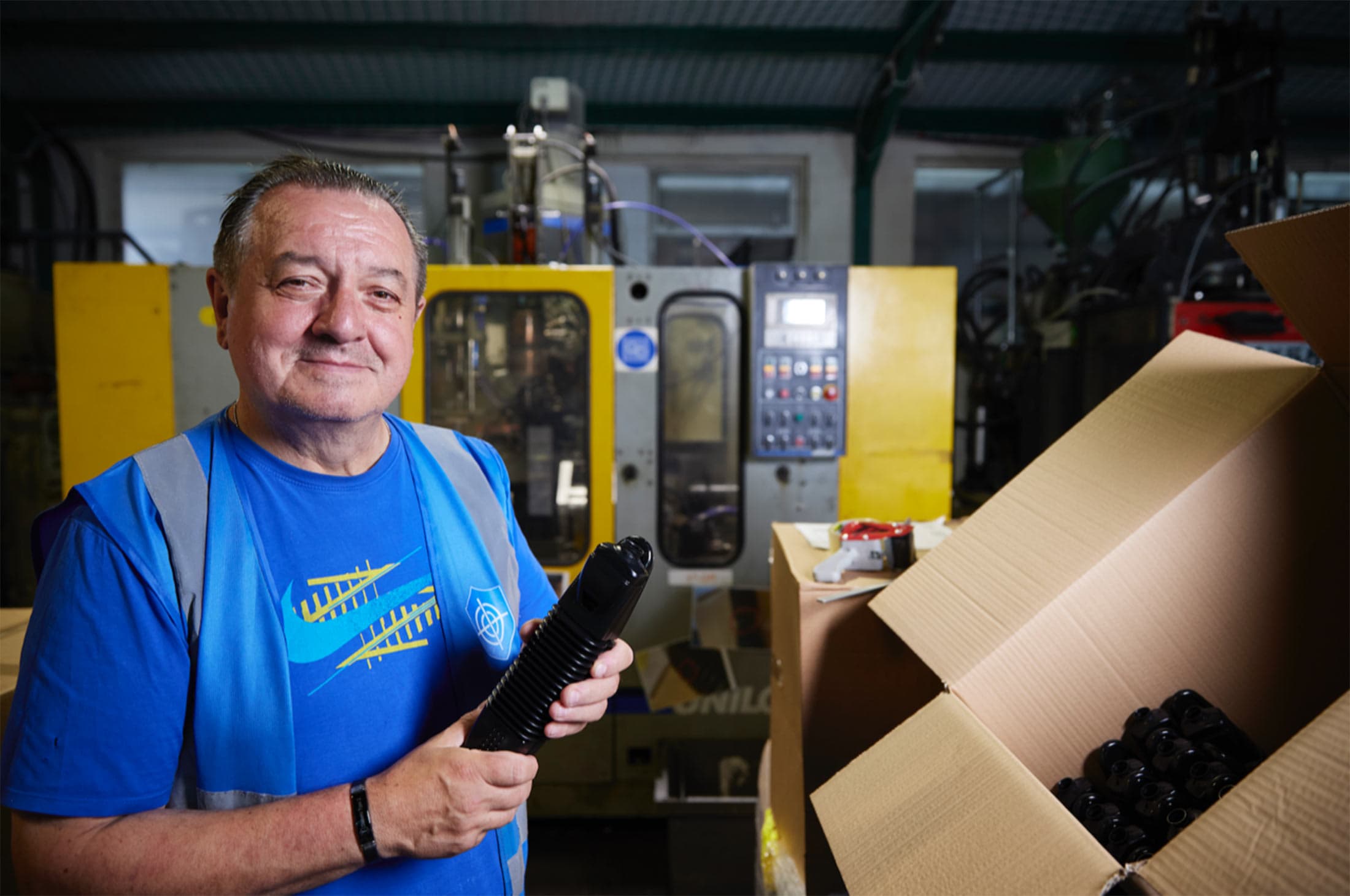 Smiling Inpress operator holding a black blow-moulded part beside a blow moulding machine