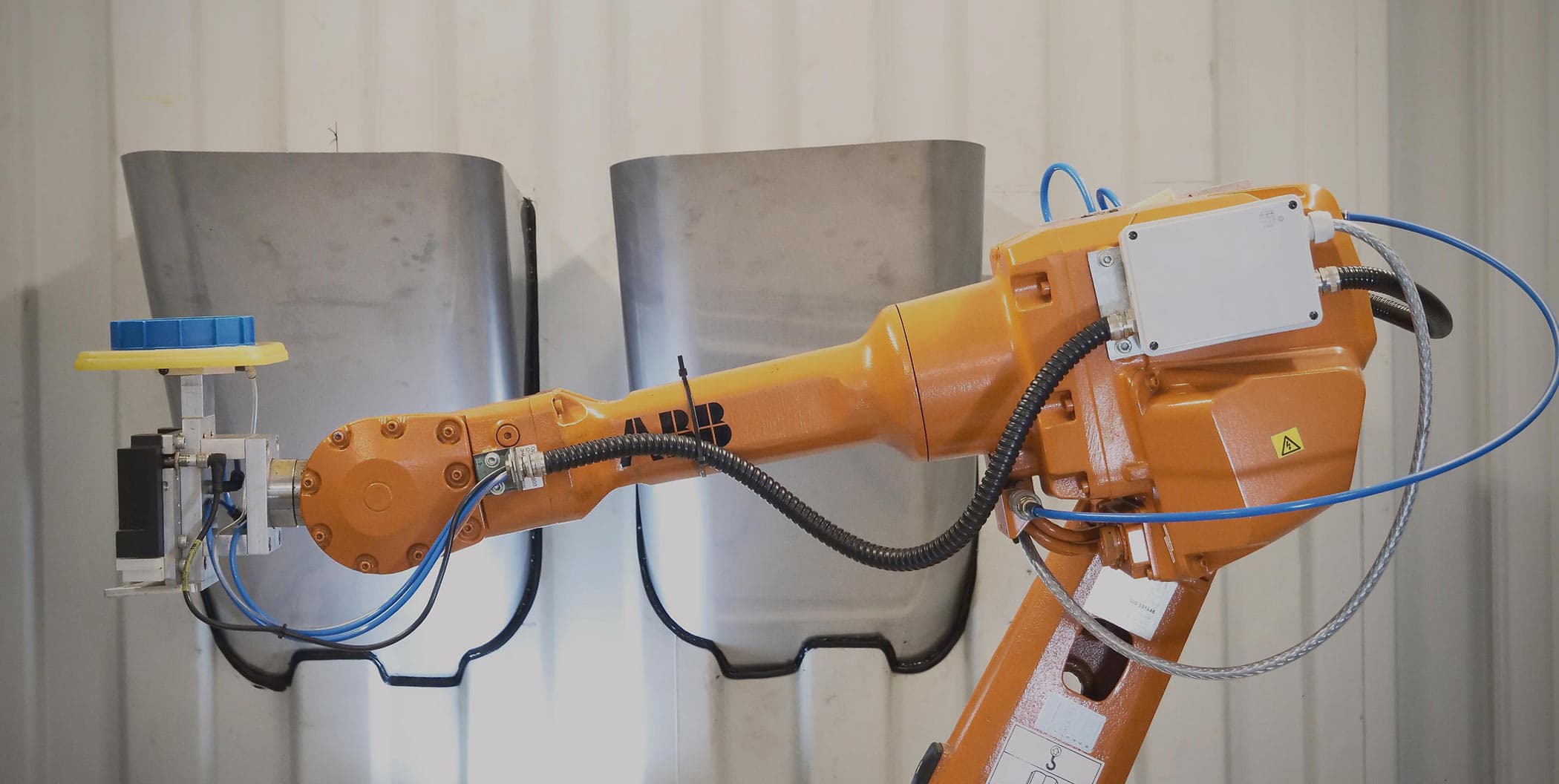Orange robot arm holding a blue moulded lid in its gripper
